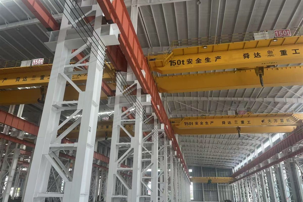Four overhead travelling cranes inside a fabricated steel workshop bay, with lattice columns and crane runway beams.
