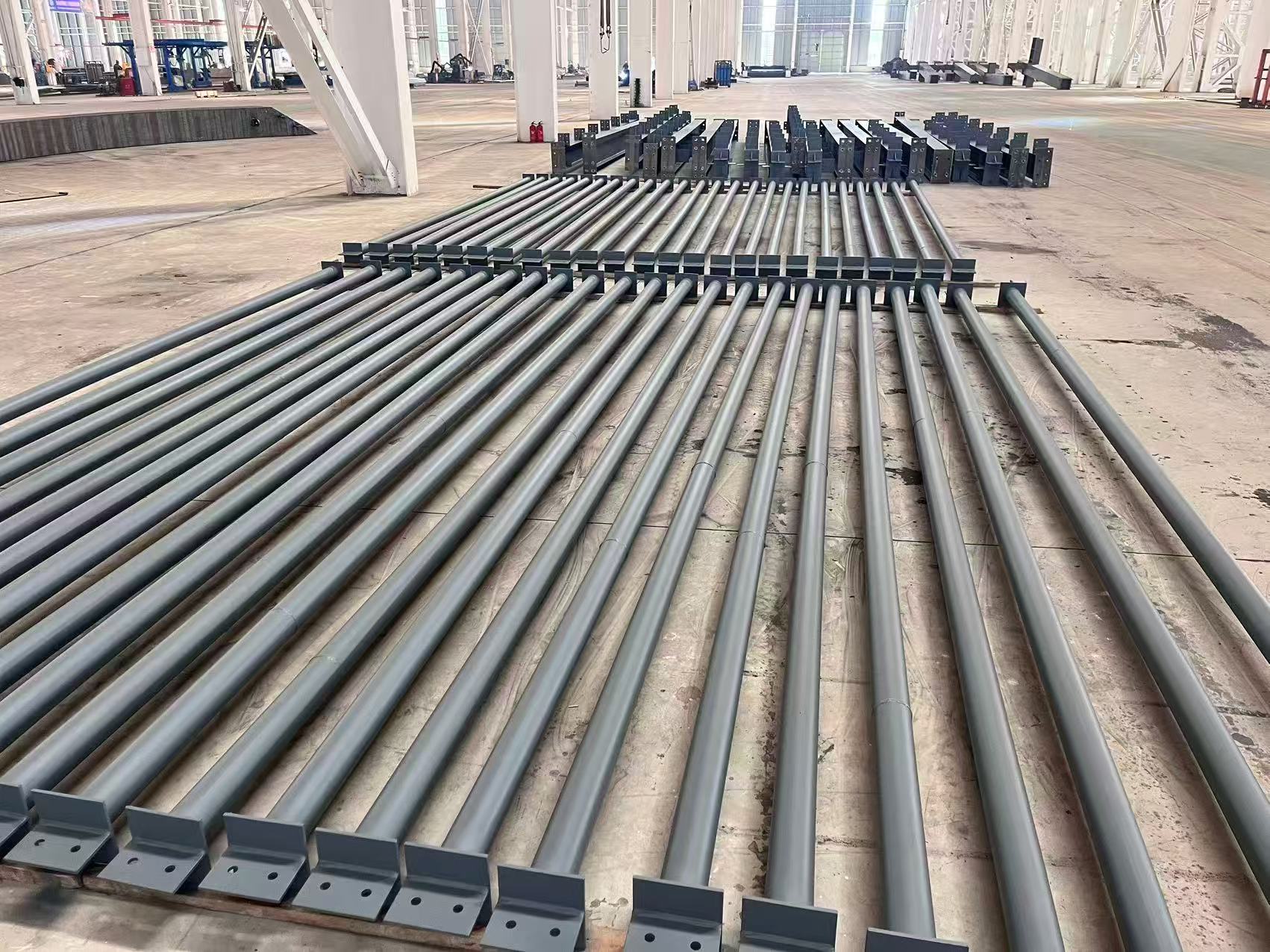 Long fabricated steel members laid out on a workshop floor with a lifting sling in the foreground and crane runway behind.