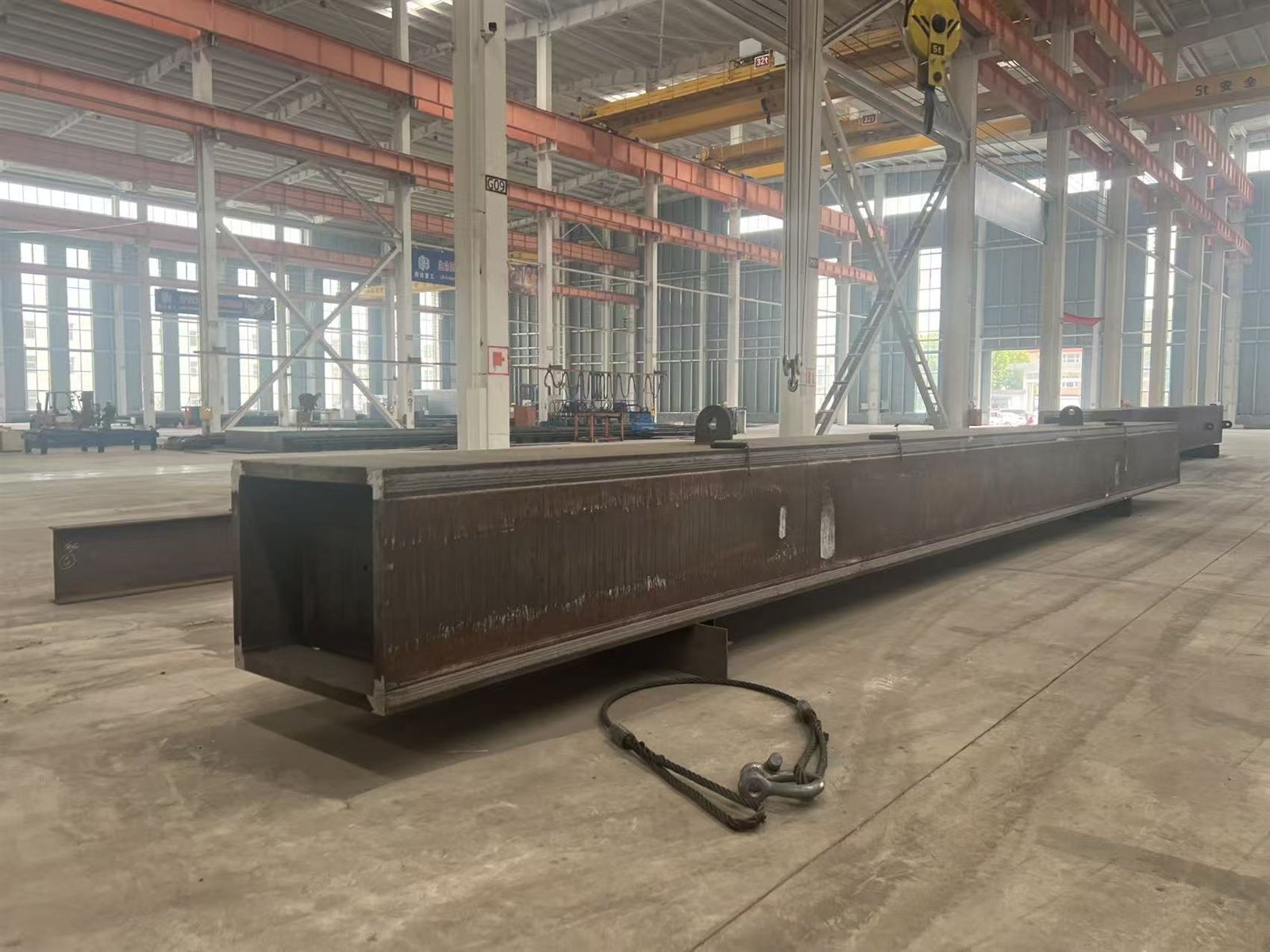 A fabricated box girder standing on the workshop floor beside its lifting gear.